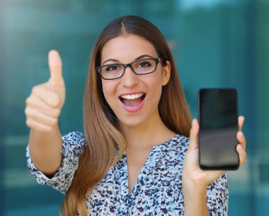 Heyecanlı iş kadını onu akıllı telefon ve başparmak gösterir.