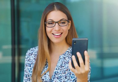 Akıllı telefon kullanarak görüntülü görüşme yapan genç kadının dış mekan portresi.