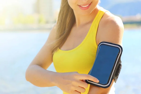 Braçadeira esportiva para smartphone. Menina desportiva tocando seu telefone inteligente antes do treino de fitness ao ar livre na praia . — Fotografia de Stock