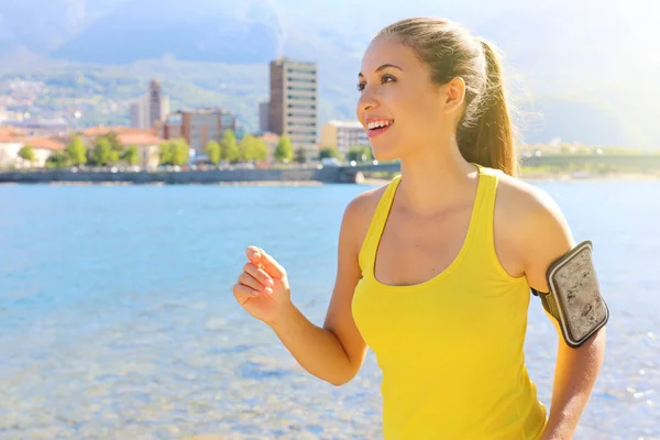 Fitness młoda atrakcyjna biegacz kobieta z opaską na telefon treningu przez jezioro miasta. Kopiuj przestrzeń. — Zdjęcie stockowe