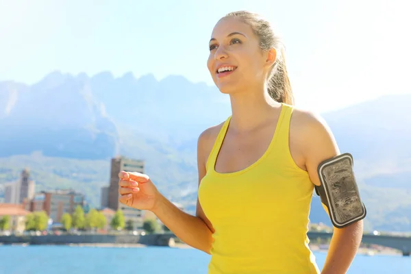 Fitness jeune femme coureuse attrayante avec bande de bras pour l'entraînement téléphonique au bord du lac de la ville . — Photo