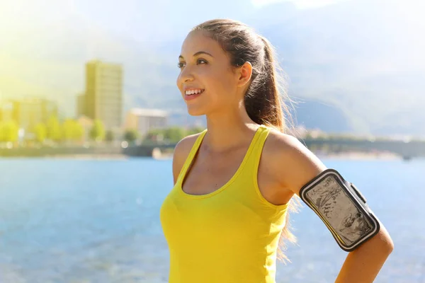 Mujer de fitness con brazalete para la tecnología del teléfono haciendo ejercicio de maratón correr estiramiento caliente en la mañana en el lago de la ciudad . — Foto de Stock