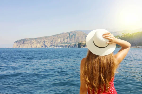 Καλοκαιρινές διακοπές στην Ιταλία. Πίσω όψη της νεαρής γυναίκας που κρατά το καπέλο της με τη χερσόνησο Sorrento στο παρασκήνιο, ακτή Σορέντο, Ιταλία. — Φωτογραφία Αρχείου