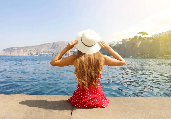 Mulher bonita com chapéu sentado na borda olhando para a deslumbrante aldeia panorâmica de Sorrento na Península Sorrentina, Itália . — Fotografia de Stock