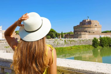 İtalya 'da tatiller. Roma, İtalya 'daki güzel turist kızın arka manzarası. Çekici moda kadını köprüdeki Castel Sant Angelo kalesine bakıyor..