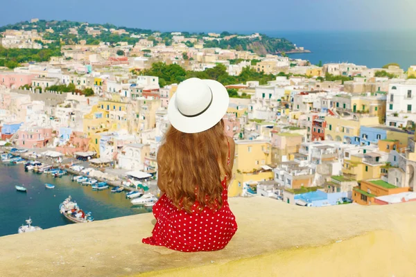 Reizen in Italië. Achteraanzicht mooie jonge vrouw met hoed op muur kijkend naar prachtig panoramisch uitzicht op het eiland Procida, Napels, Italië. — Stockfoto