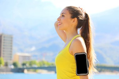 Akıllı telefon kolu bandı boş, sabah şehir gölünde temiz hava soluyan bir fitness kadınının yan görüntüsü. Boşluğu kopyala.