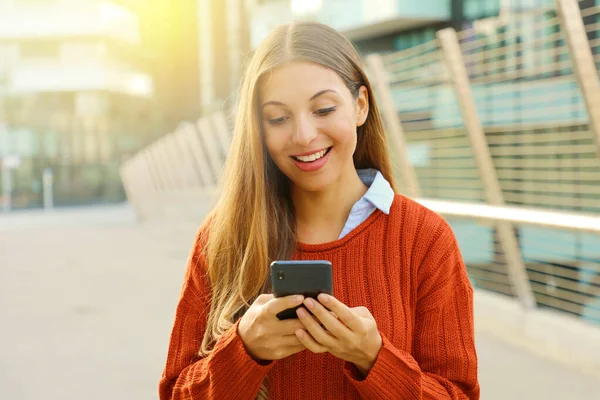 Счастливая молодая женщина с помощью смартфона в солнечный день осенью на открытом воздухе в современном городе . — стоковое фото