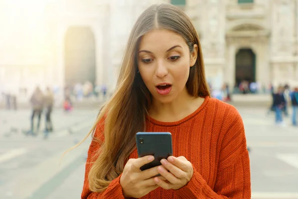 Chica sorprendida mira el teléfono móvil en la plaza de la ciudad en otoño . —  Fotos de Stock