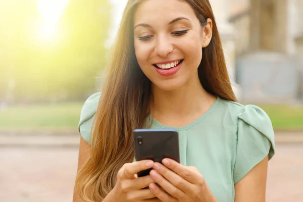 Primer plano de hermosa mujer sonriente escribiendo en el teléfono inteligente al aire libre . — Foto de Stock