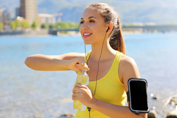 Szomjas fitness nő nyílik üveg vizet edzés után kültéri. Fit nő használ smartphone fitness app karszalag a tevékenység Tracker. — Stock Fotó