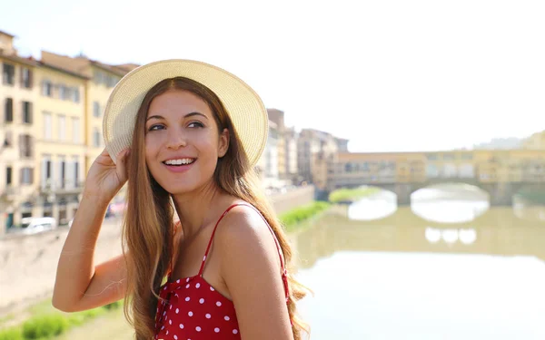 Prachtig lachend meisje in Florence met Ponte Vecchio brug en Arno rivier op de achtergrond. Portret van een jonge vrouw met hoed en jurk op bezoek in Toscane in Italië. — Stockfoto