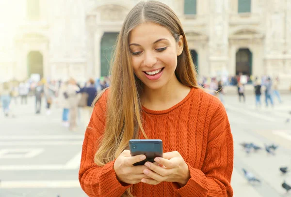 Feliz mujer alegre mirando su teléfono inteligente en la plaza de la ciudad . — Foto de Stock