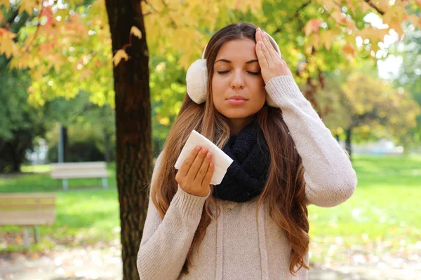 Young woman suffering headache cold fever holding paper tissue outdoors. — ストック写真