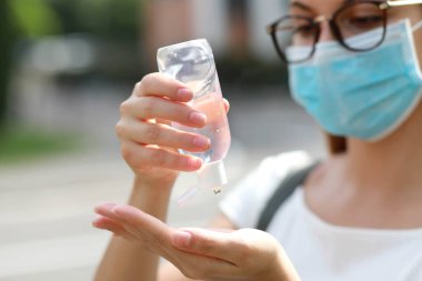 Şehir caddesinde el dezenfektanı jeli tıbbi maskeli bir kız. Antiseptik, Hijyen ve Sağlık Hizmetleri konsepti. Ellere odaklan..