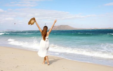 Kollarını kaldırıp rüzgarın tadını çıkaran özgür mutlu kız ve uçurtma uçuran insanlar, Corralejo Dunes plajı, Fuerteventura, Kanarya Adaları