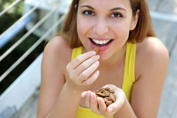 Close up of fitness girl eating almonds in the park. Healthy food concept.