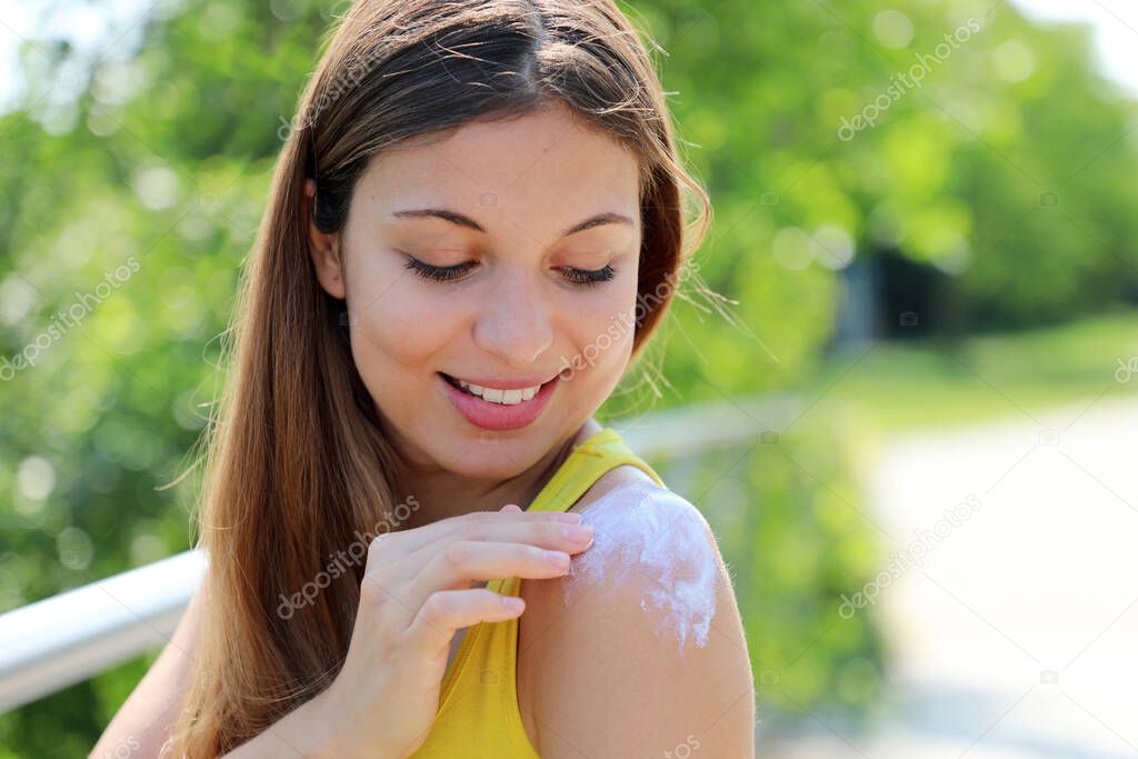 Happy young woman applying sunblock on shouder skin outdoor on a summer day
