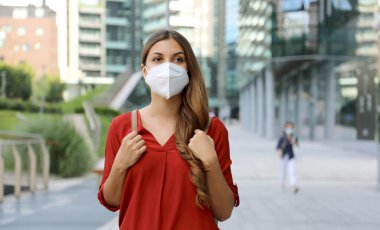 Modern şehir caddesinde yürüyen koruyucu maske takan genç kadın KN95 FFP2. Coronavirus hastalığına karşı yüz maskeli öğrenci kız 2019 (COVID-19).