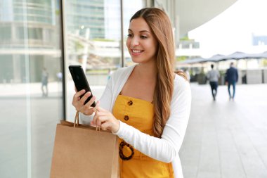 Alışveriş torbaları ve akıllı telefonları olan moda alışverişçisi kadın.