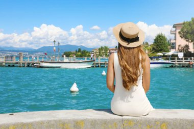 İtalya 'da tatiller. Duvarda oturup Garda Gölü 'ndeki Sirmione Limanı' nın keyfini çıkaran güzel bir kızın arka görüntüsü. İtalya 'da yaz tatilleri.