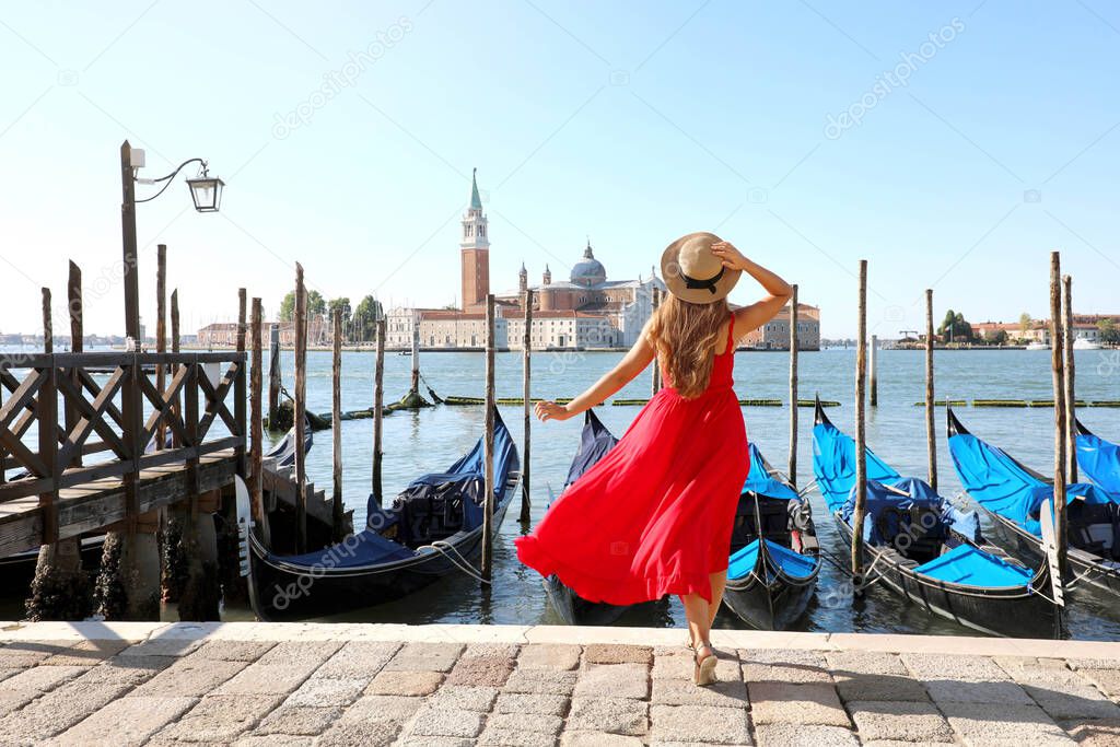 Holidays in Venice. Back view of beautiful girl in red dress enjoying view of Venice Lagoon with the island of San Giorgio Maggiore and gondolas moored.
