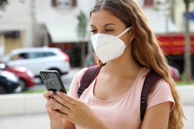 Şehir caddesindeki akıllı telefonla koruyucu maske takan kız öğrencilerin fotoğraflarını çek.