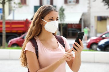 Akıllı telefonlu Brezilyalı kadın sokakta yüz koruyucu maske takıyor.