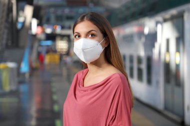 Metro trenini bekleyen sıradan bir kadının portresi metro istasyonunda KN95 FFP2 koruyucu maskeyle.