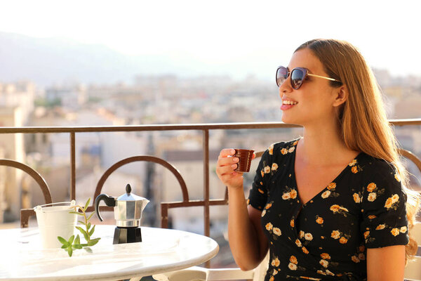 Portrait of beautiful woman with sunglasses sitting on terrace drinking Italian coffee at sunset