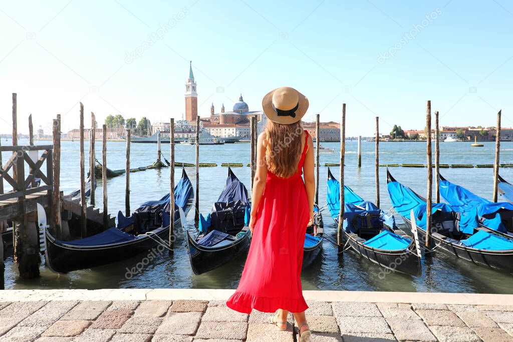 Holidays in Venice. Back view of beautiful girl in red dress enjoying view of Venice Lagoon with the island of San Giorgio Maggiore and gondolas moored.