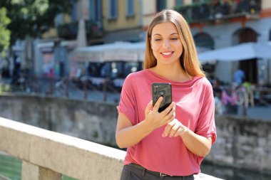 Gülümseyen genç kadın İtalya 'nın Milano kentindeki Navigli kanallarında cep telefonuyla sohbet ediyor.