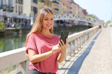 Gülümseyen genç kadın İtalya, Milano 'da sohbet etmek için akıllı telefon uygulamasında mesajları kaydırıyor