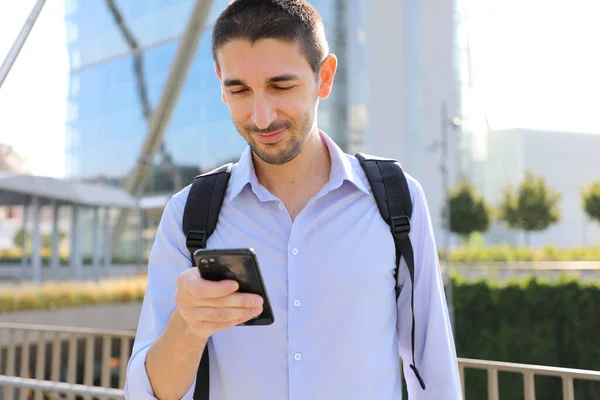 Young urban businessman using smartphone app texting sms message in city street