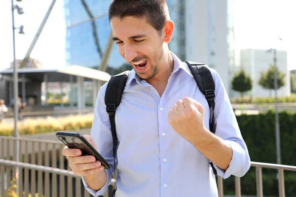 兴奋的年轻人在智能手机上查好消息 大学生手持手机在现代城市街道上欢庆 — 图库照片