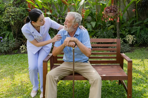 Senior man zitten en glimlachende verpleegster, neemt zorg en discussie — Stockfoto
