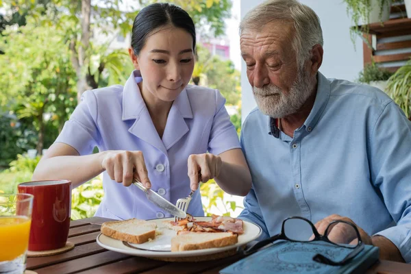 Senior man geluk met lachende verpleegster, neemt zorg ontbijt in Stockfoto