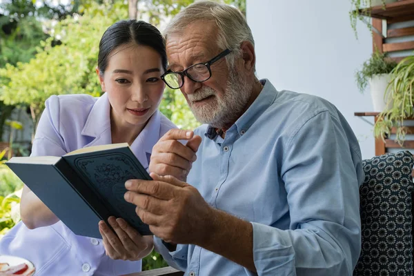Senior man geluk met lachende verpleegster, leesboek samen bij b — Stockfoto