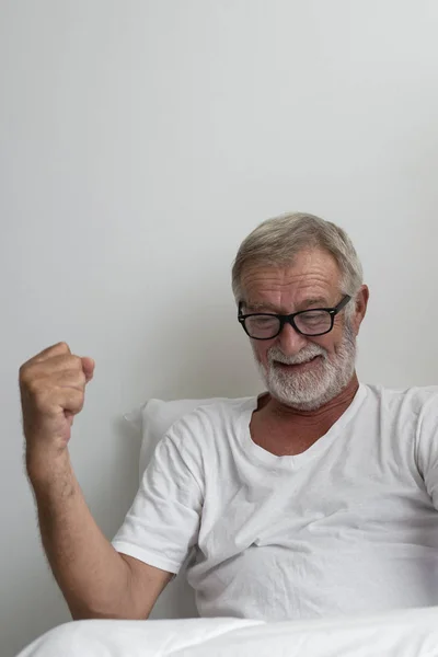 白い部屋でベッドの上で笑顔と歓声を持つシニアの男性 — ストック写真