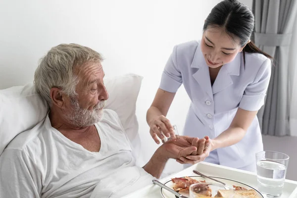 Sjuksköterska ge piller till Senior man efter frukost och diskussion om — Stockfoto
