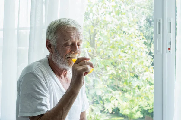 先輩男性はオレンジジュースのグラスを持ち、考え、見ているo — ストック写真