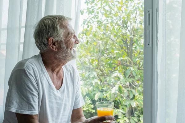Hombre mayor mantenga vaso de jugo de naranja y pensar y mirar o — Foto de Stock