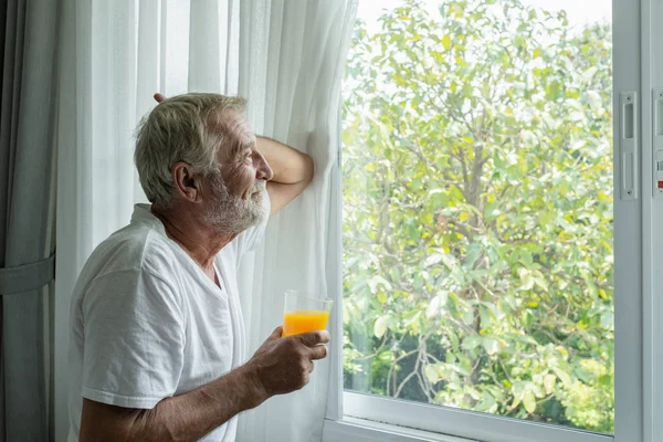 Starszy mężczyzna trzymać szklankę soku pomarańczowego i myślenia i patrząc o — Zdjęcie stockowe