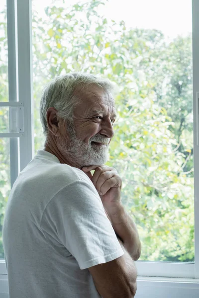 Hombre mayor sonriendo y pensando con felicidad en la habitación blanca — Foto de Stock