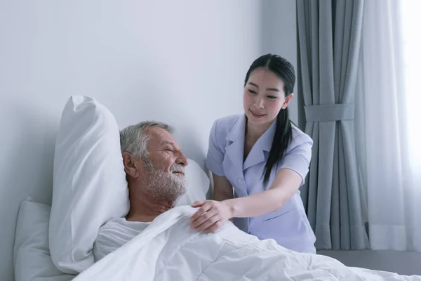Senior man met lachende verpleegster, neemt zorg en discussie op bed Stockafbeelding