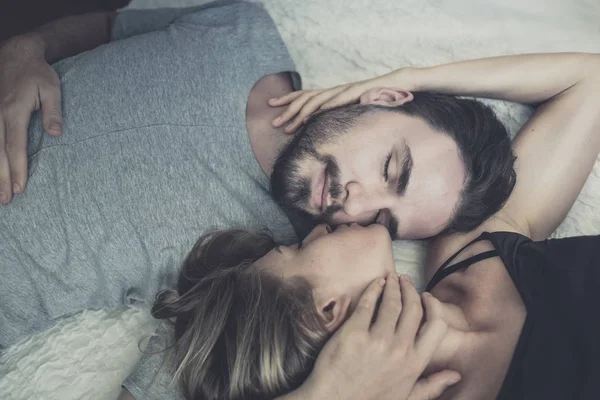 Liefdevolle gelukkig paar in liefde glimlach en kus haar wang op het bed, — Stockfoto