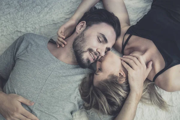 爱幸福的夫妇在爱微笑和亲吻她的脸颊在床上, 免版税图库图片