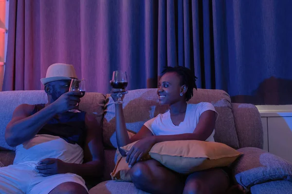 Usměvavý muž a žena držící sklenici vína sedící na pohovce v t — Stock fotografie