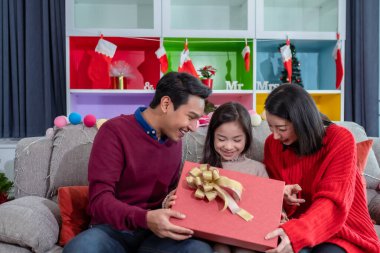 Mutlu Asyalı aile kızı, baba ve anne birlikte büyük bir hediye açarlar ve yılbaşı günü Noel ağacı ile süslenmiş oturma odasında sürpriz yaparlar.
