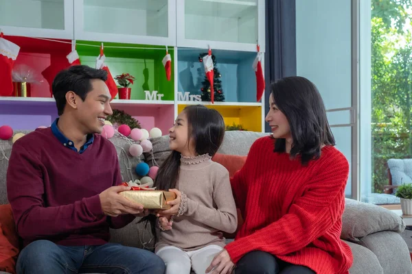幸せなアジアの娘の笑顔は クリスマスの祭りの日のために木で飾られたリビングルームでクリスマスの日に一緒に与えられ 祝う父の母親と贈り物を保持します — ストック写真